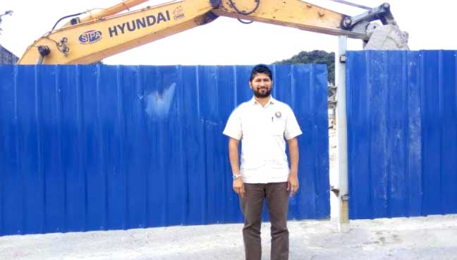 PSM's Suresh stands in front of a fence that blocks an area where buses used to park.